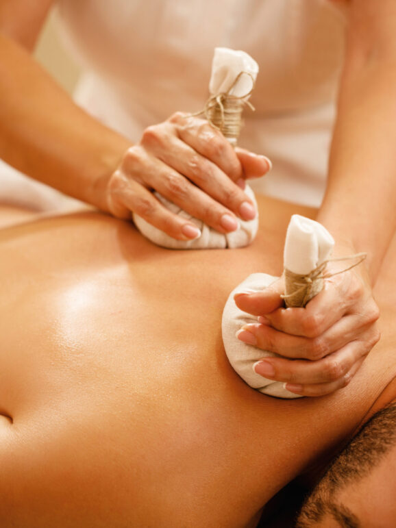 Close-up of man getting back massage with detox herbal balls at health spa.