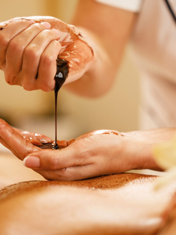 Close-up of massage therapist pouring hot chocolate in her hands before spa treatment.
