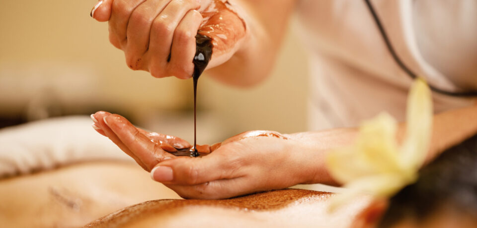 Close-up of massage therapist pouring hot chocolate in her hands before spa treatment.