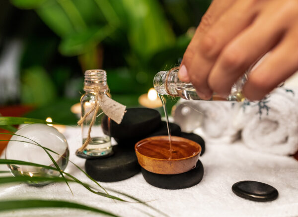 A man pours oil from a jar of essential oils standing on stones for a therapy stone and located on a terry towel next to which are transparent spheres, a twisted terry towel of white color and a sprig of lavender