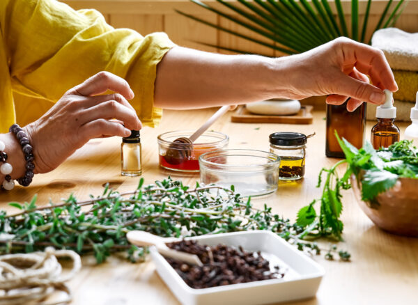 Woman prepares aromatherapy session at the table with essential oil diffuser medical herbs, different types of oils and essences. Aromatherapy and alternative medicine concept. Natural remedies.