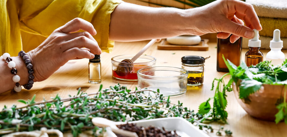 Woman prepares aromatherapy session at the table with essential oil diffuser medical herbs, different types of oils and essences. Aromatherapy and alternative medicine concept. Natural remedies.